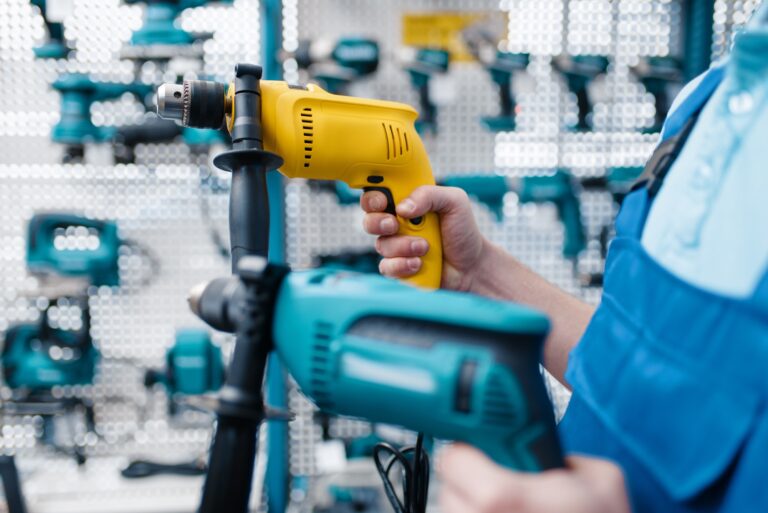 Worker holds two electric drills in tool store